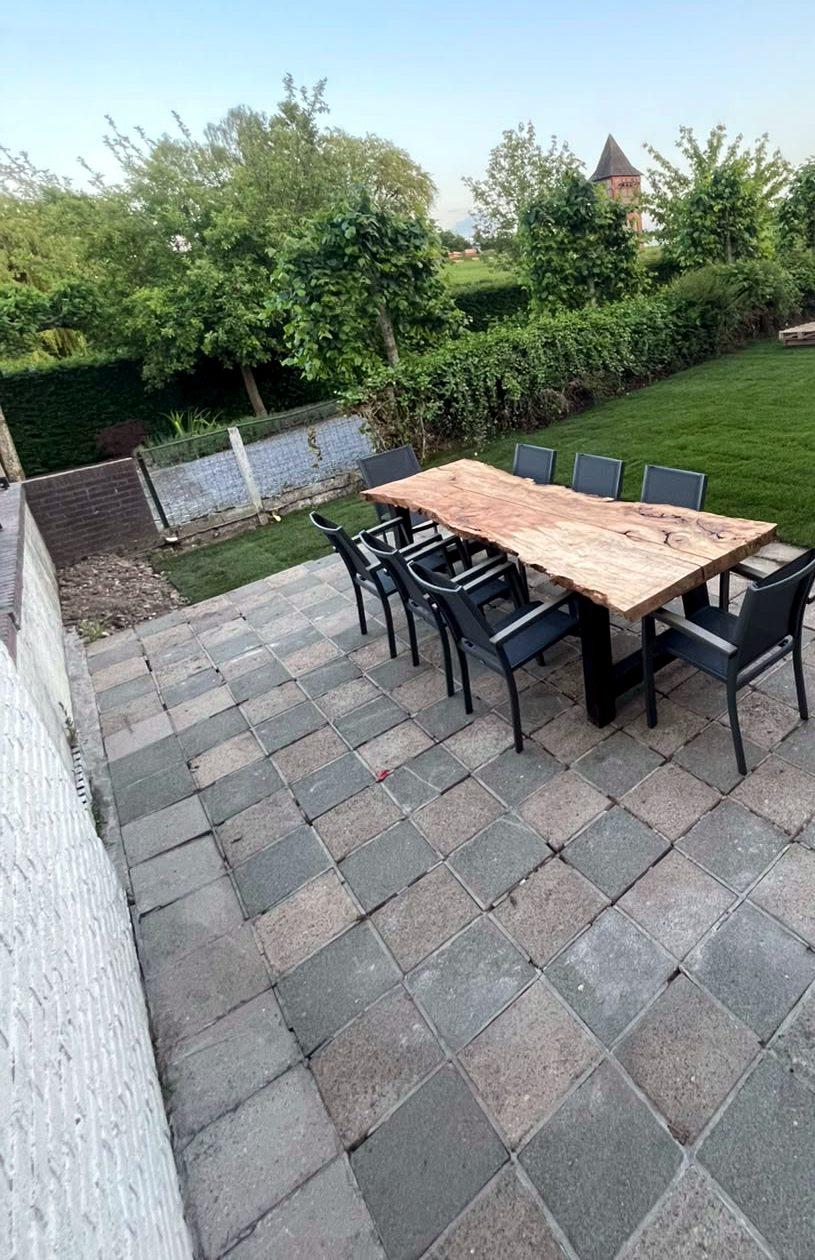 Terras met grote houten buitentafel en tuin met zicht op de velden van de Voerstreek
